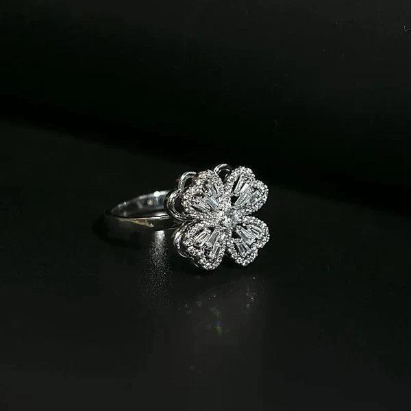 Silver floral ring with four heart-shaped petals and sparkling gemstones on black background
